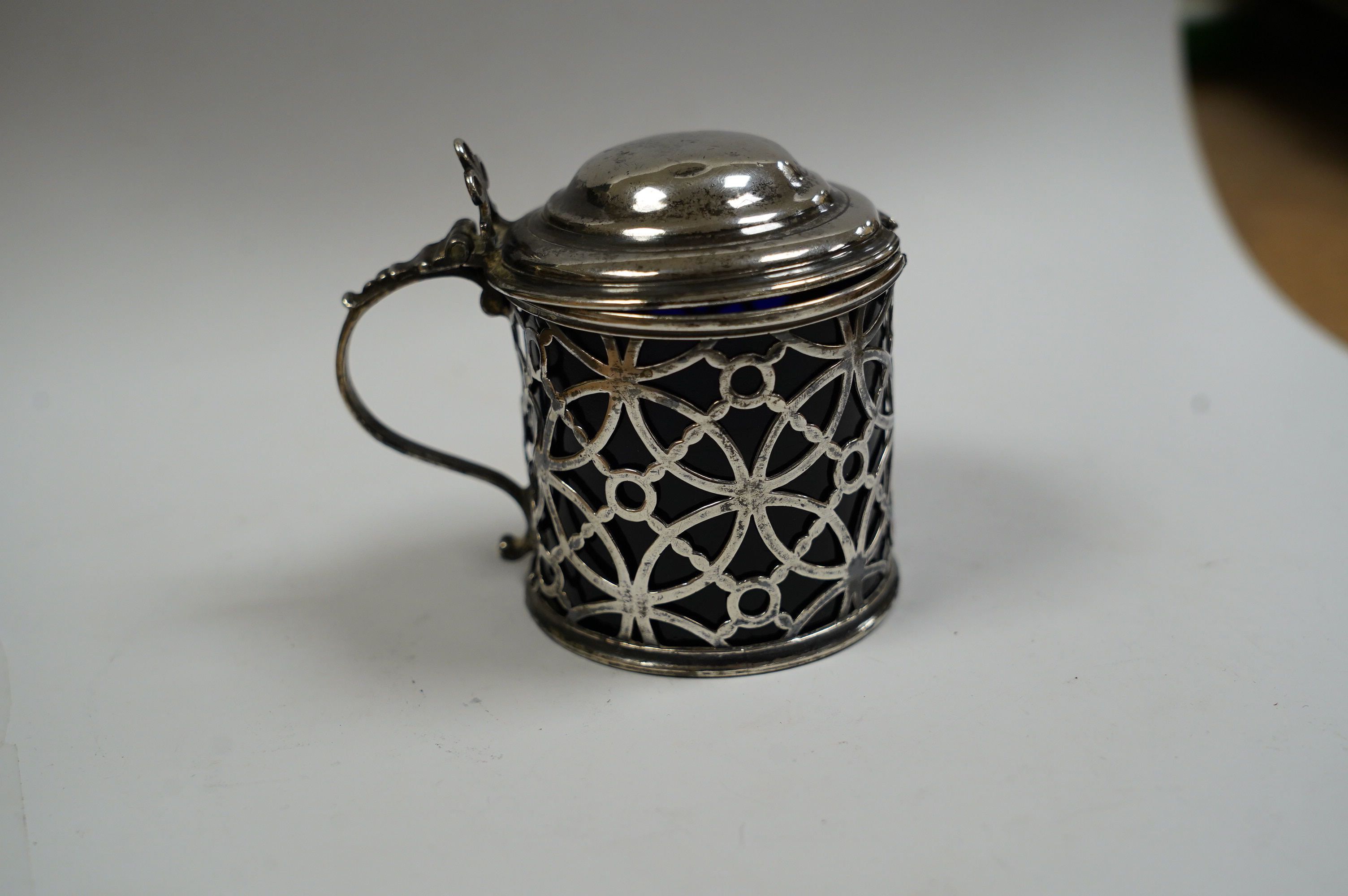 A George III pierced silver drum mustard pot, Aldridge & Green, London, 1767, height 70mm lid unmarked, with blue glass liner, later associated silver spoon. Condition - poor to fair